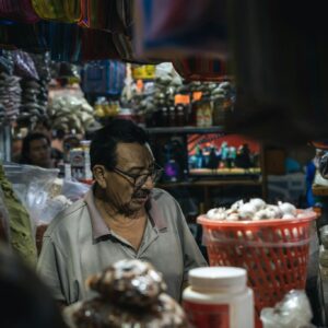 A man selling goods at a vibrant market stall, surrounded by diverse merchandise.