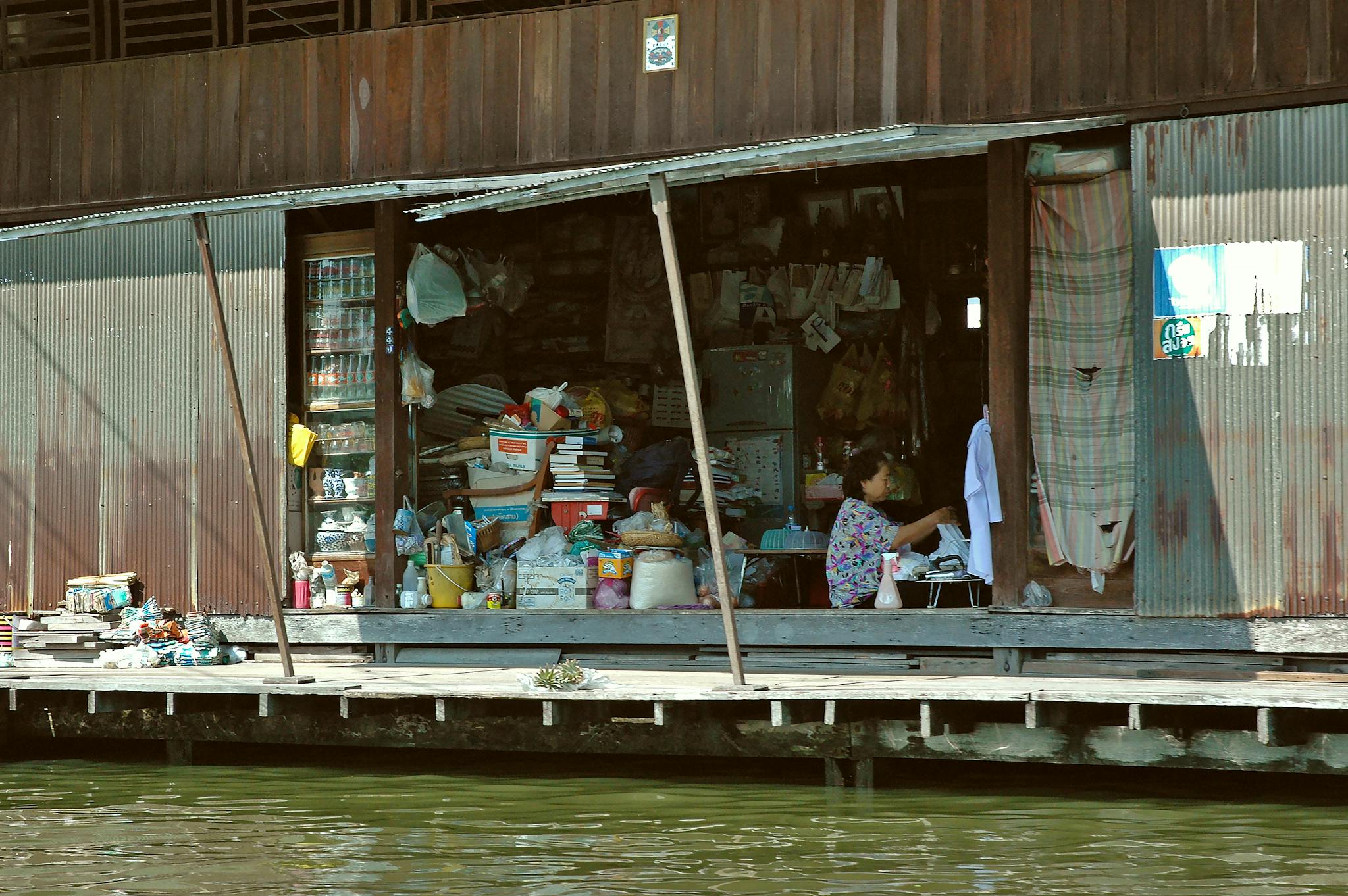 Asian woman working inside a cluttered store on a waterside urban setting.