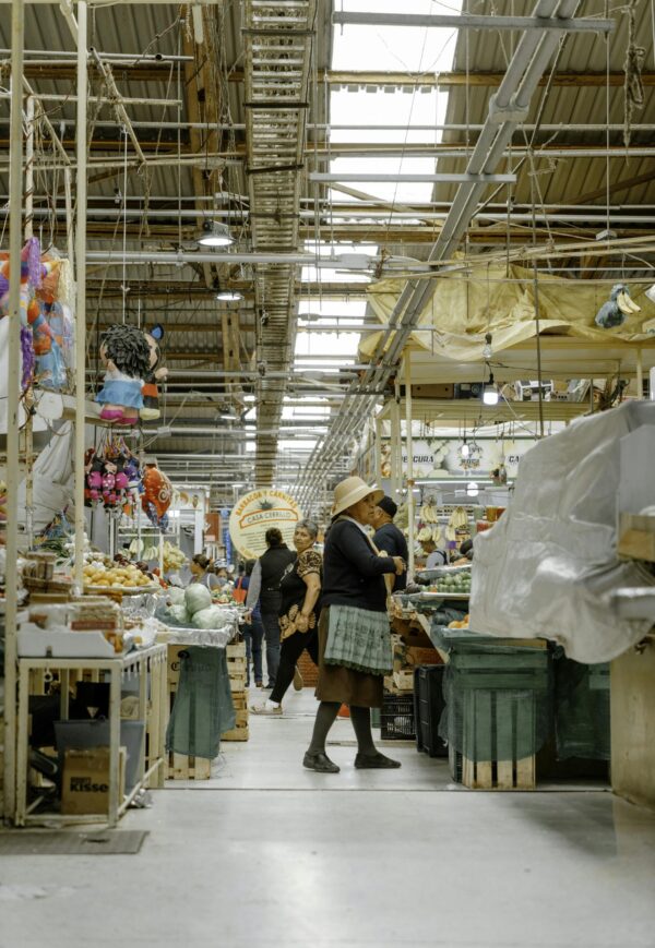 Lively indoor marketplace scene with diverse shoppers exploring various stalls and products.